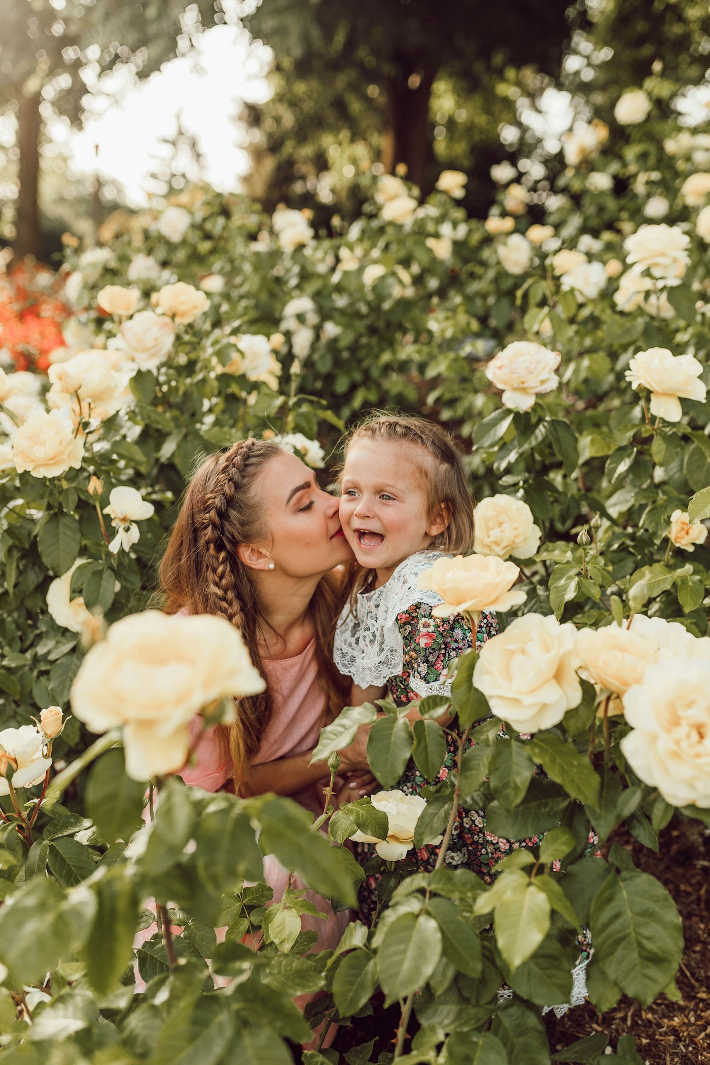 Madre besando la mejilla de su hija entre rosas blancas